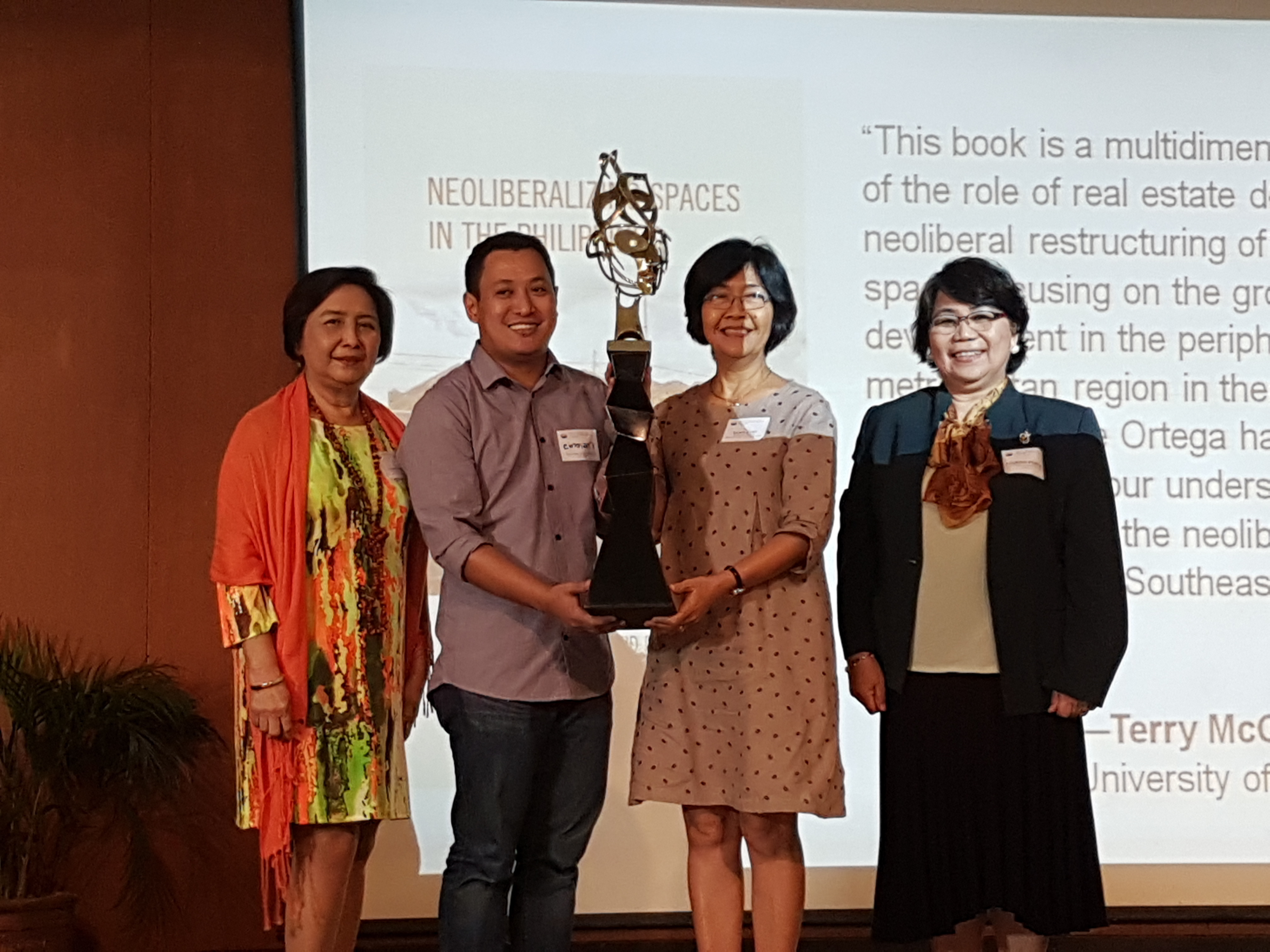 <br />
Mr. Emmanuel B. Garcia of the UP Department of Geography and Prof. Grace T. Cruz of UPPI hold Dr. Ortega’s trophy. Flanking them are PSSC Executive Director Amaryllis T. Torres (left) and PSSC Chairperson Lourdes M. Portus  (right).